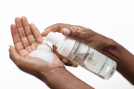 Bilden visar en person som pumpar ut ett l&ouml;dder fr&aring;n en flaska Dermaceutic Advanced Cleanser i handen. Bakgrunden &auml;r vit.