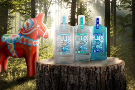 En grupp Flux munsk&ouml;ljprodukter (Mild Mint, Aloe Vera och Original Coolmint) st&aring;ende p&aring; en tr&auml;stubbe i en skogsmilj&ouml; med en svensk dalah&auml;st i bakgrunden. Produkten &auml;r f&ouml;rpackad i 100% &aring;tervunnen plast.